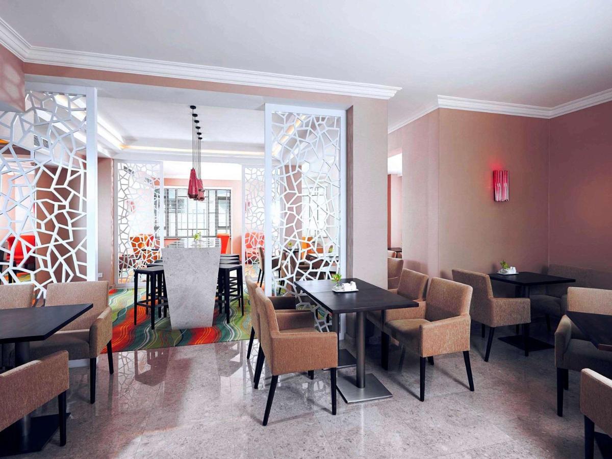 Paradox Singapore Merchant Court At Clarke Quay Exterior foto The photo shows a modern restaurant interior. There are several tables arranged with dark surfaces and comfortable beige chairs. The walls are painted in neutral tones, and there are decorative partition screens with an abstract pattern that adds a c